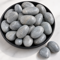Gray polished spa stones in a black bowl on a white marble surface.