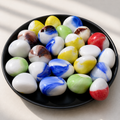 A collection of colorful marbled glass pebbles in white, blue, yellow, green, red, and brown swirls, arranged in a black ceramic dish on a light beige surface.